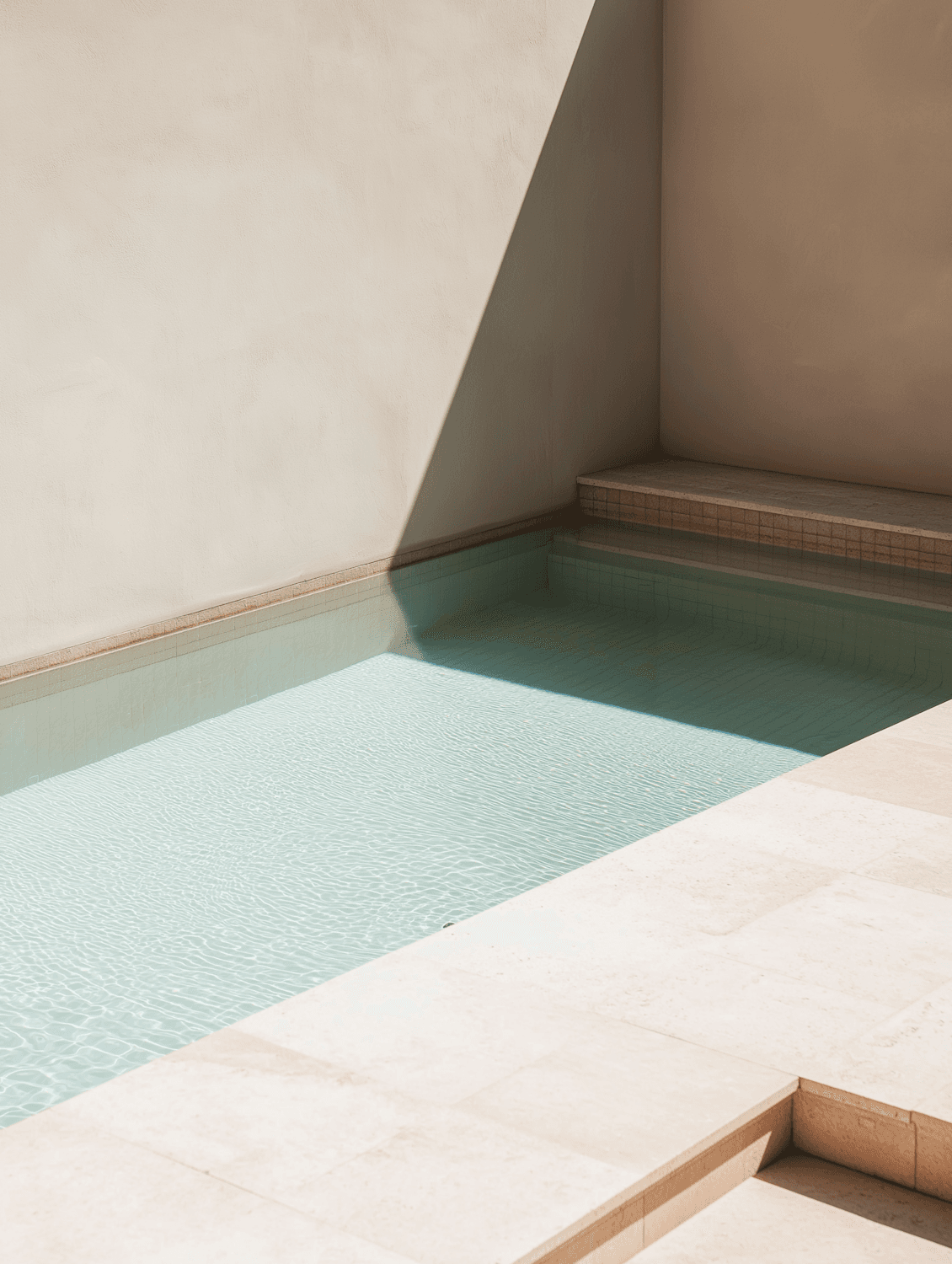 A still outdoor pool edged in pale stone with a crisp line of shadow